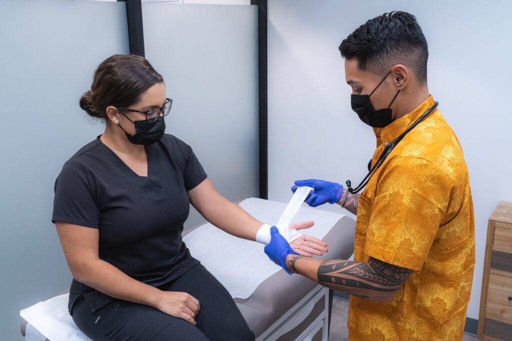 Clinician bandaging a patient’s wrist in an exam room.