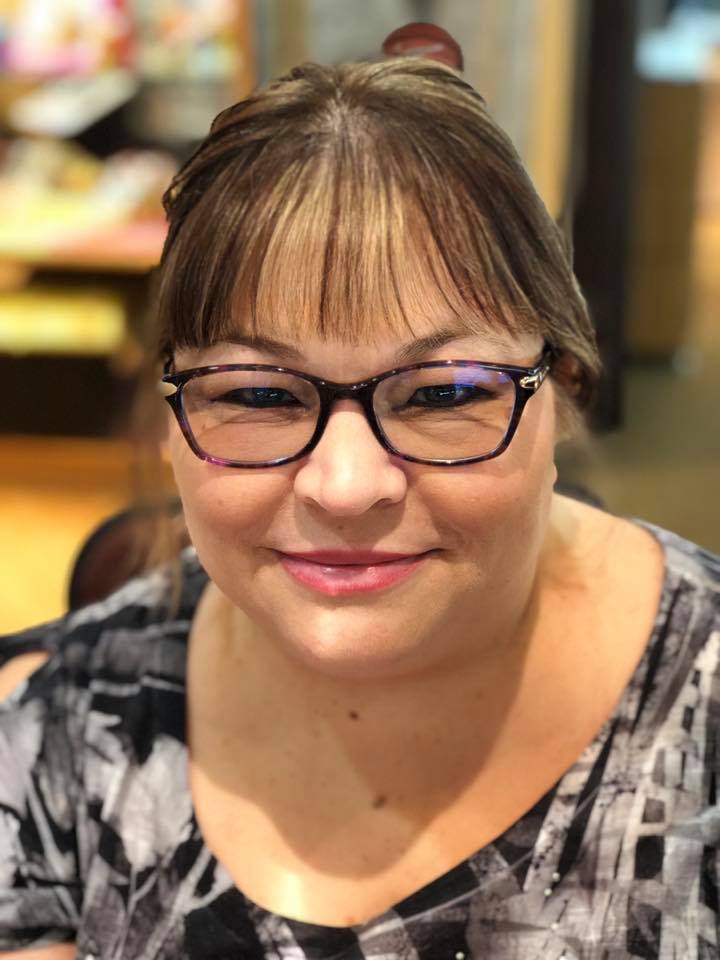A woman smiling at the camera, wearing dark-framed glasses and a light sweater