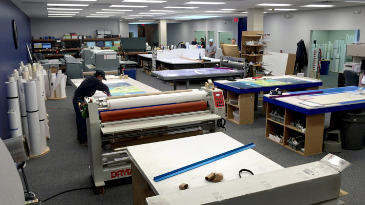 Printing workshop with wide-format printers and supply shelves.
